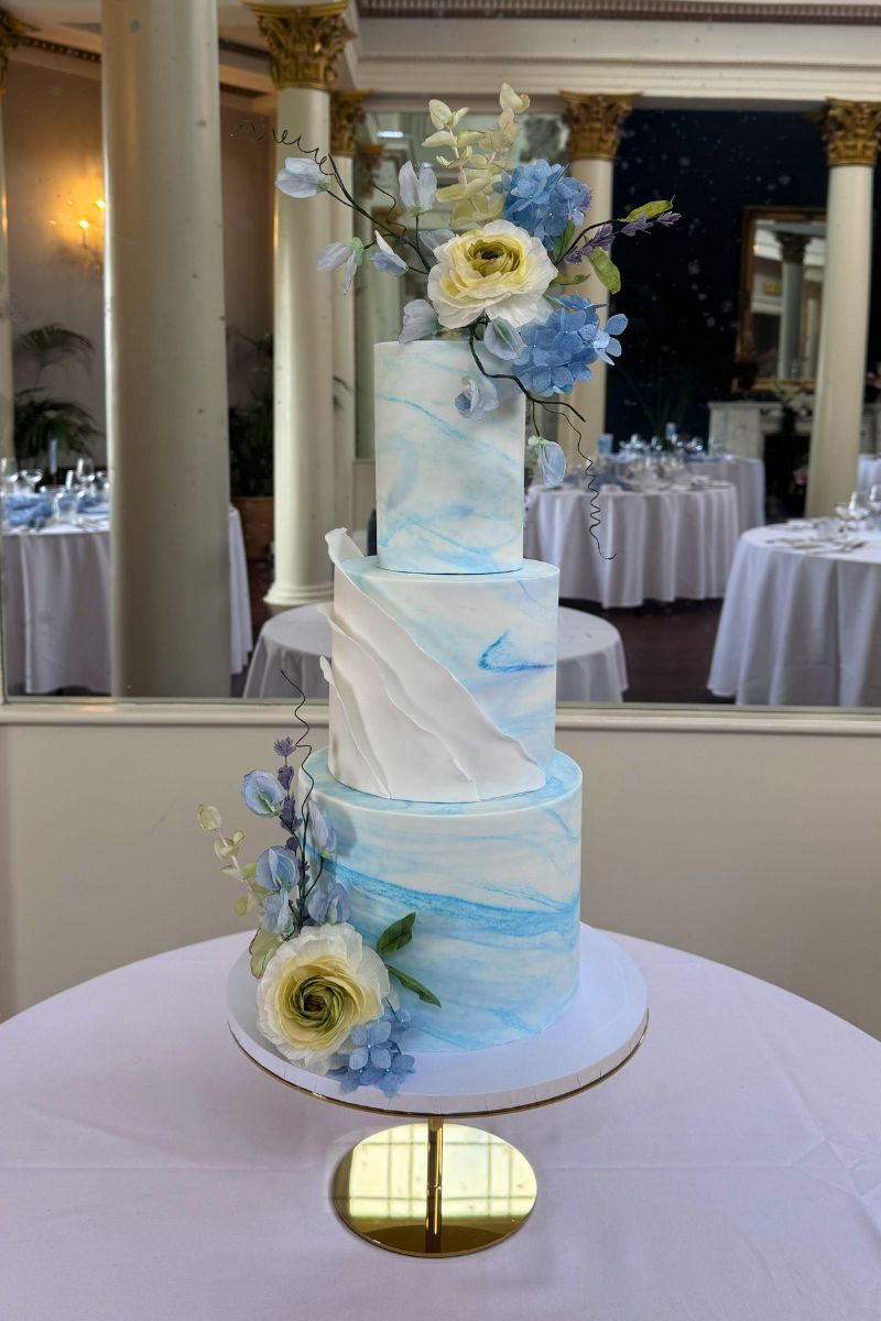 Three tier white and blue wedding cake with handmade wafer paper florals and handpainted dog